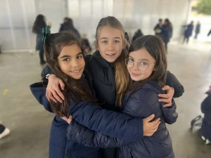 Tres alumnas sonrientes abrazadas en el patio cubierto del colegio