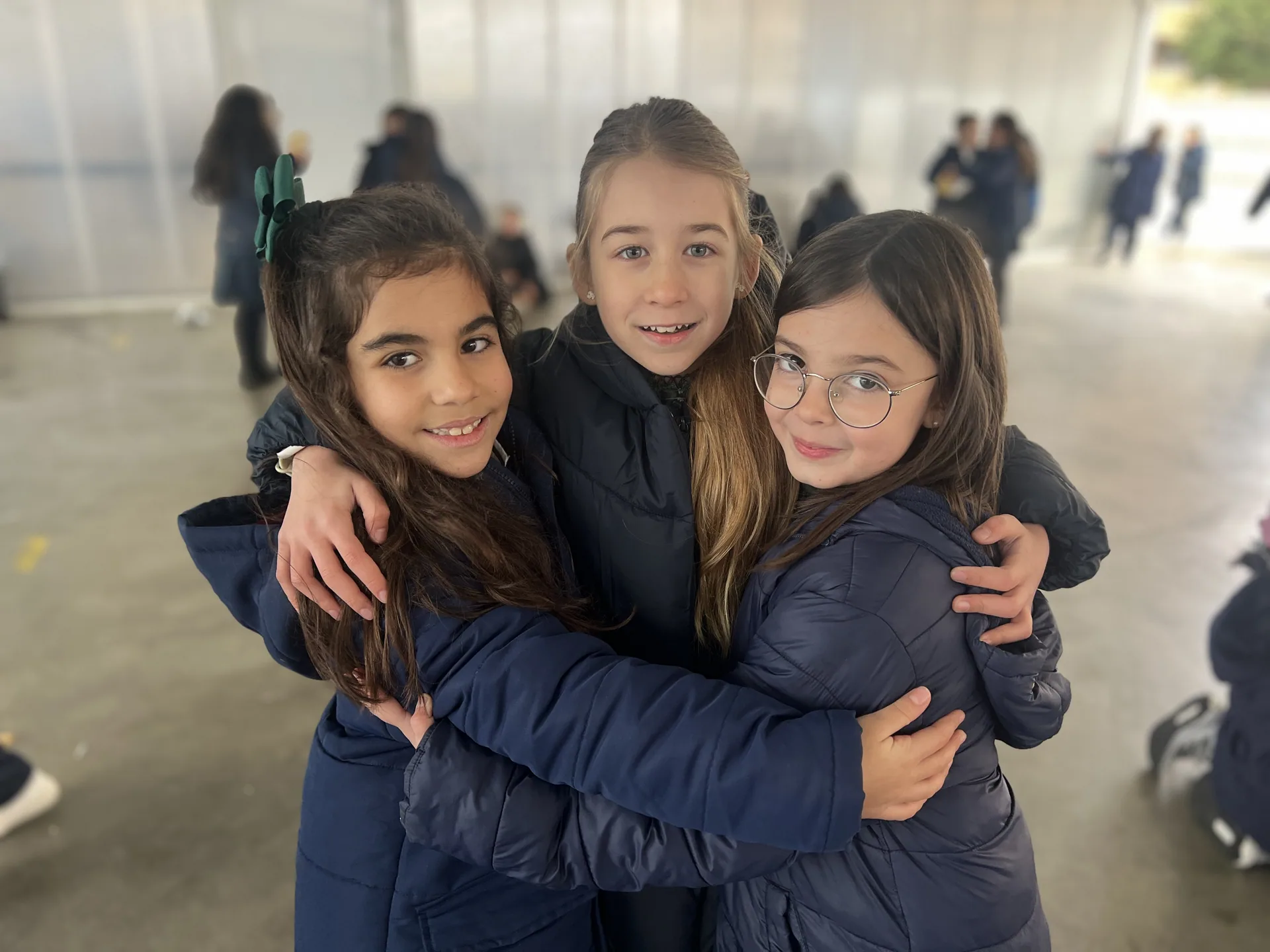 Tres alumnas sonrientes abrazadas en el patio cubierto del colegio