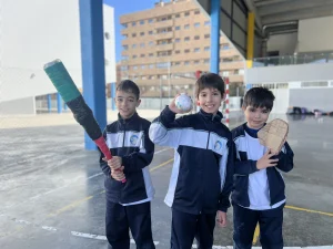 Tres alumnos con bate y pelota en el patio del colegio