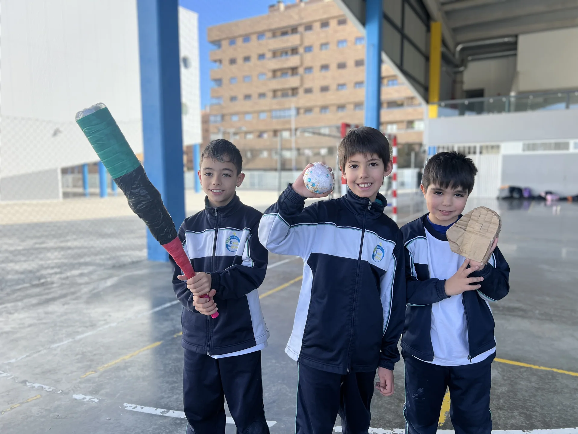 Tres alumnos con bate y pelota en el patio del colegio